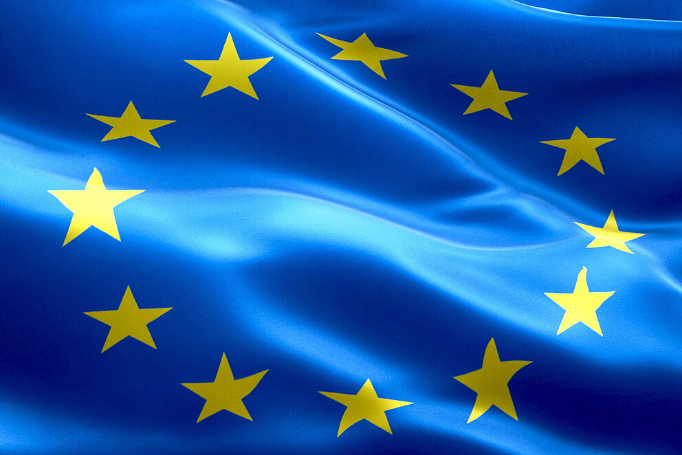 Die Flagge der EU in Blau mit einem Kreis aus gelben Sternen füllt das Bild komplett aus.