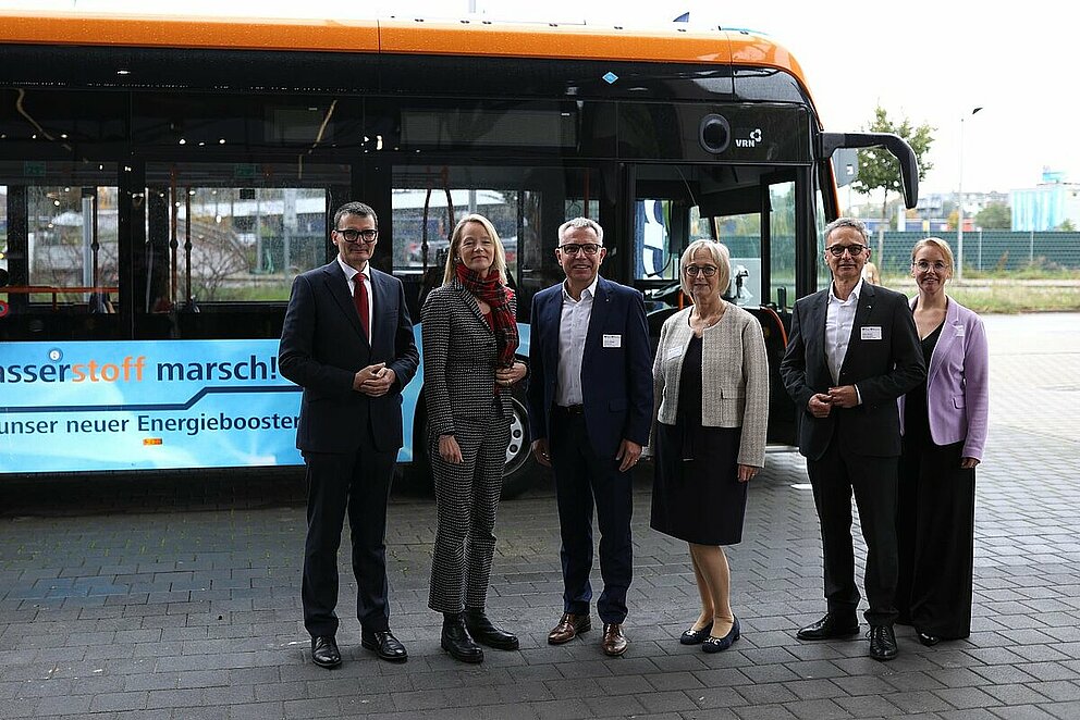 Vor einem H2-Bus des Projekts H2Rhein-Neckar stehen Staatssekretär Höppner, Ministerin Walker und Verantwortliche der MRN und e-mobil BW