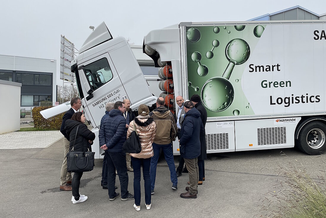 Eine Gruppe Menschen steht vor einem weißen Lkw mit Wasserstoff-Symbolen.