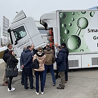 Eine Gruppe Menschen steht vor einem weißen Lkw mit Wasserstoff-Symbolen.