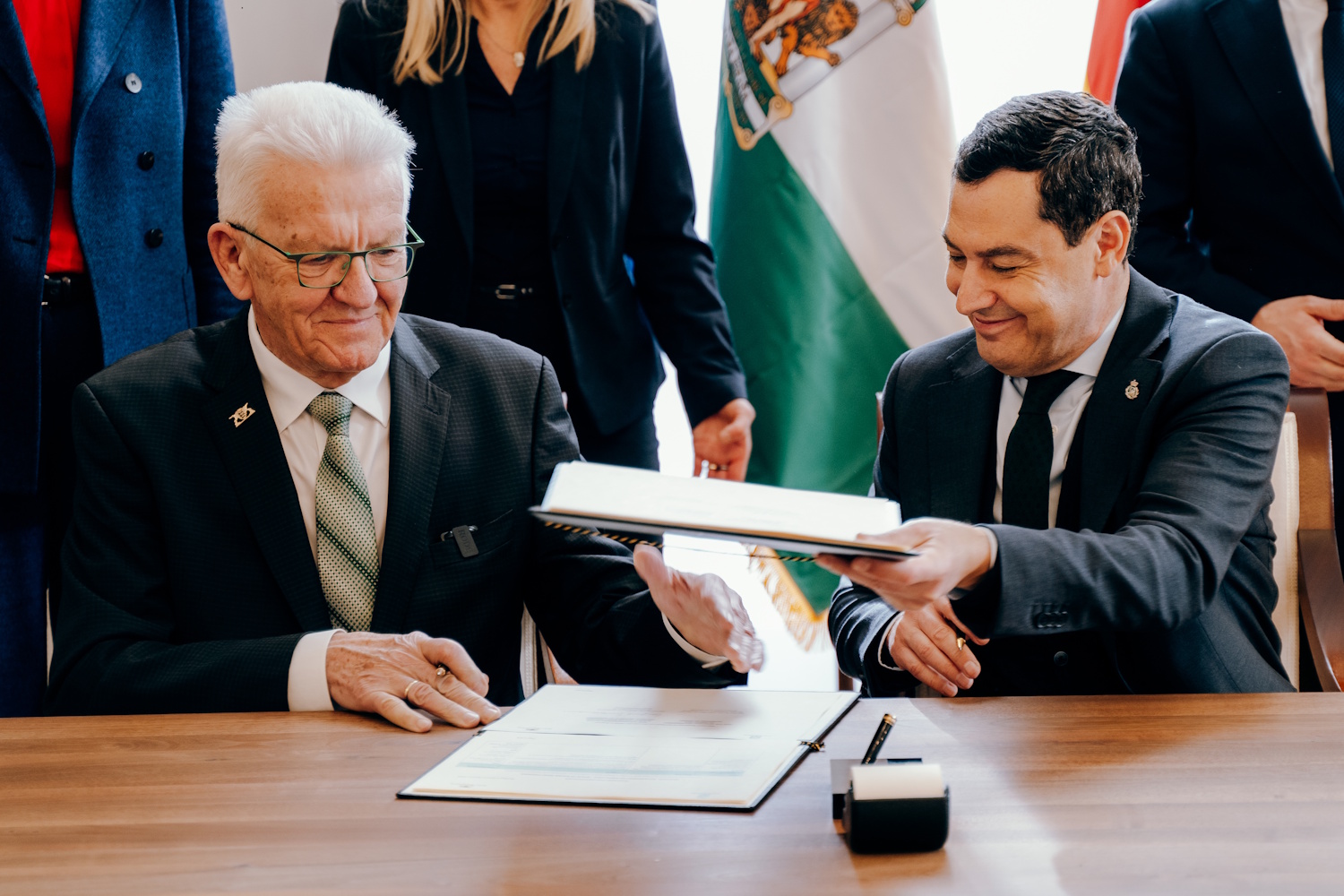 Die beiden Regierungschefs sitzen in ministerialem Setting an einem Holztisch und unterschreiben lächelnd ein Dokument.