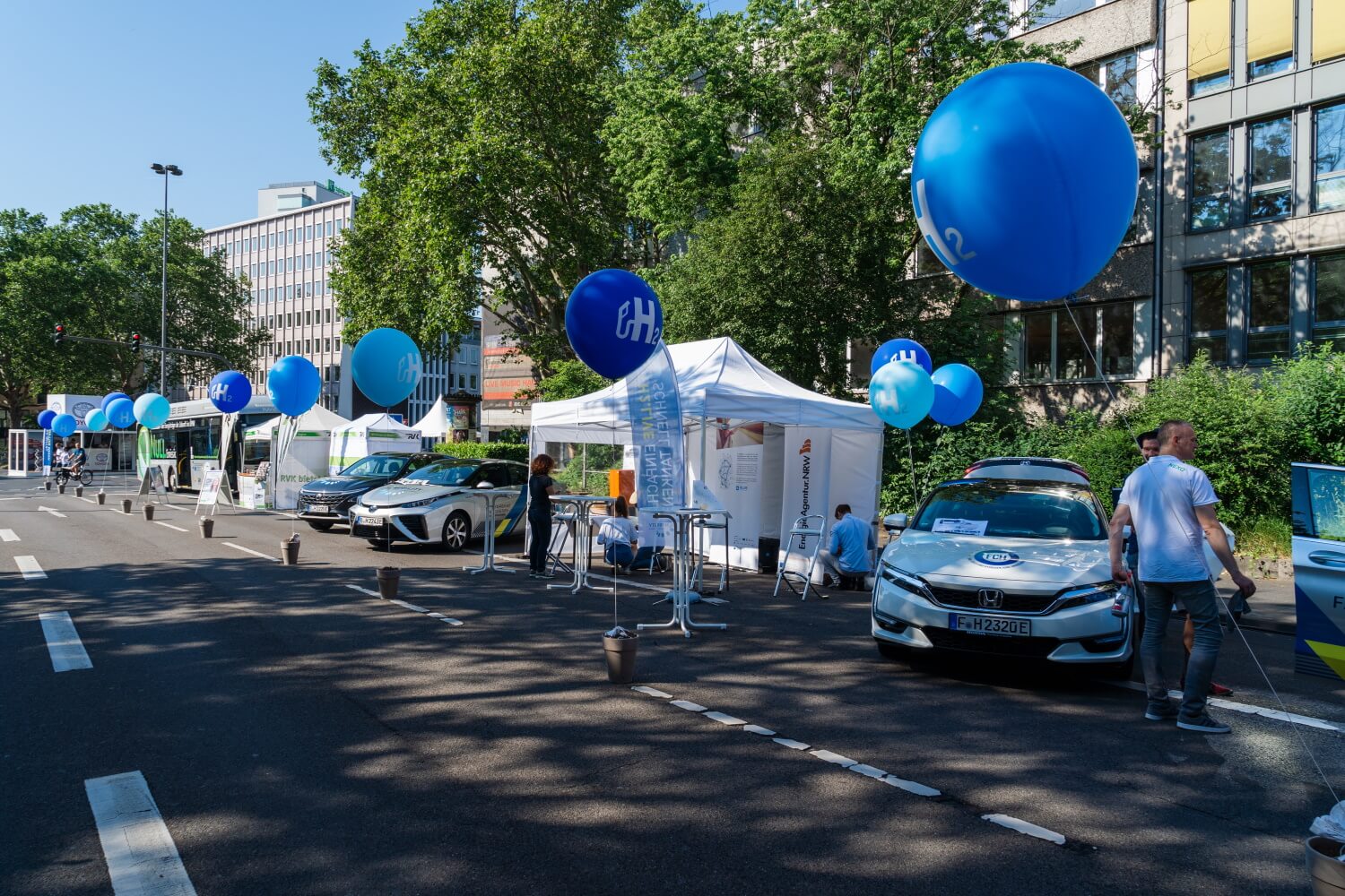 Viele weiße Pavillons, die mit blauen Ballons geschmückt sind, stehen am Straßenrand einer nicht für den Verkehr freien Straße.