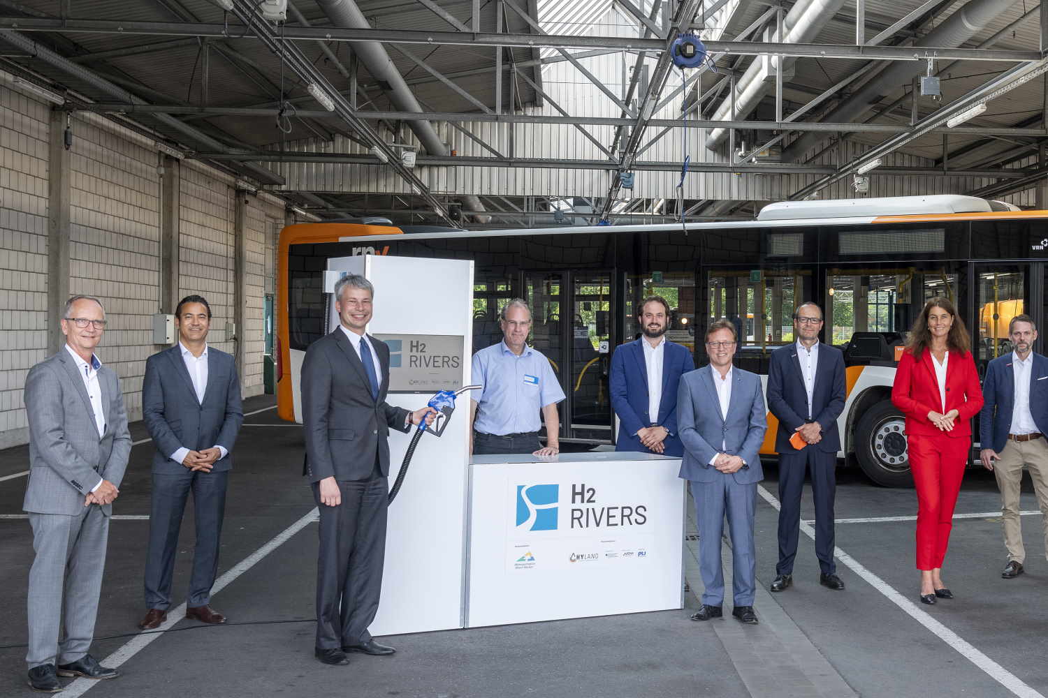 In einer Werkshalle stehen die Projektverantwortlichen vor einem Stand mit dem Logo von H2Rhein-Neckar.